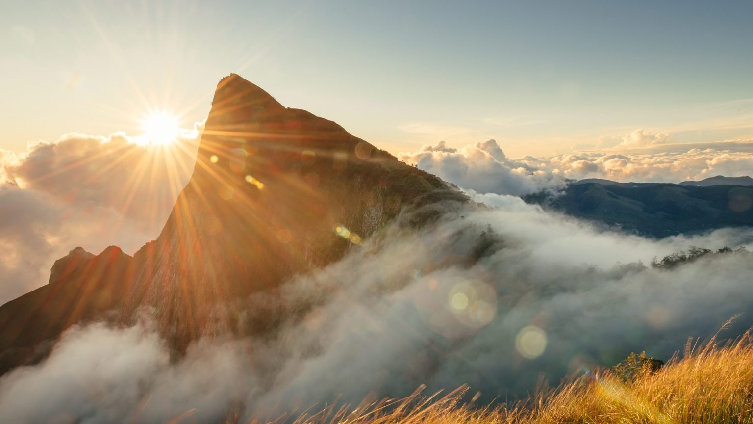 Rocky mountain peak lit by the rising sun above clouds and drifting fog