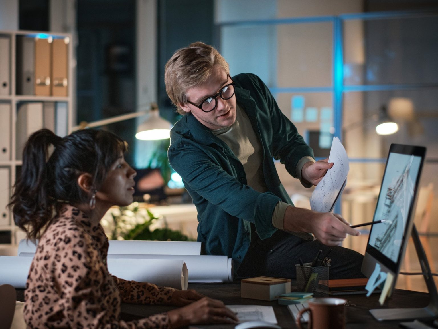 Two coworkers reviewing a design on a computer monitor late at night