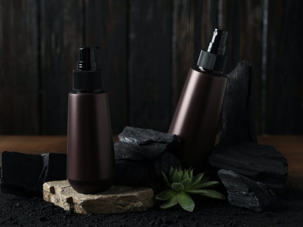 Dark cosmetic bottles styled with charcoal and a succulent