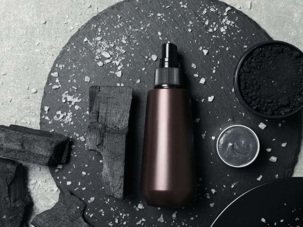Top view of a cosmetic bottle and gel jar with charcoal on a slate platter