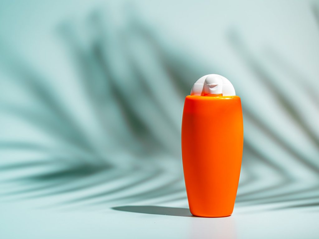 Orange bottle on a pale turquoise background with a palm leaf shadow