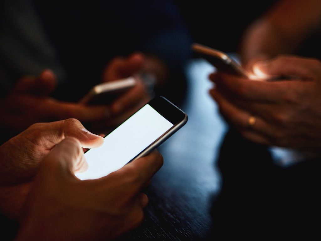 Three people using glowing smartphones together in a dark room