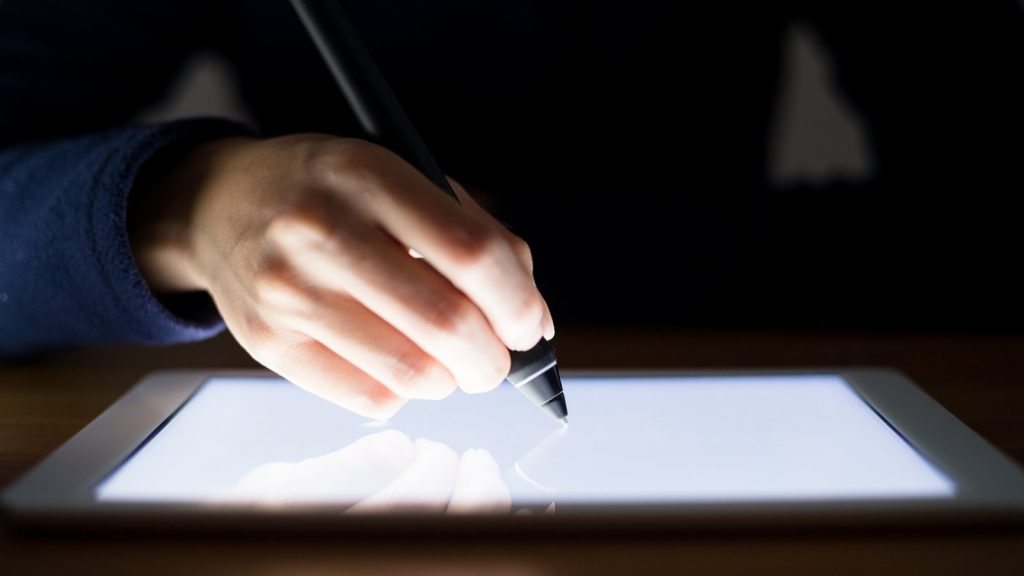 Hand drawing with a digital pen on a glowing tablet in a dark room