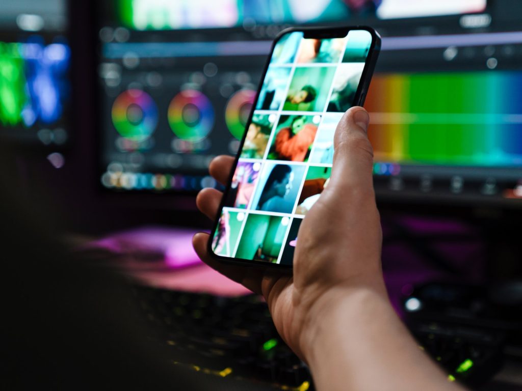 Hand holding a phone with a colourful photo grid on screen in a dark room