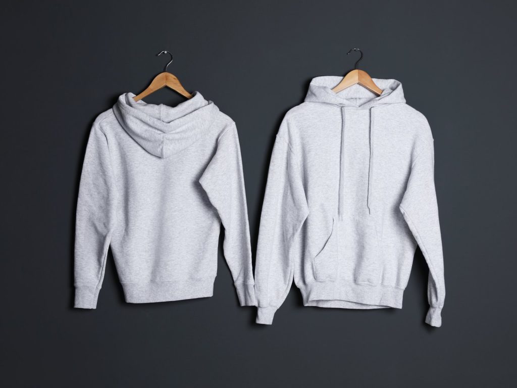 Two blank grey hoodies on hangers against a dark grey wall