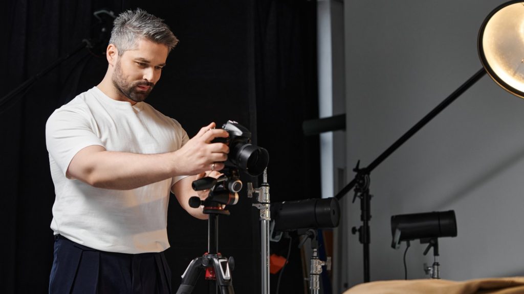 Photographer adjusting a camera on a tripod in a dark photo studio